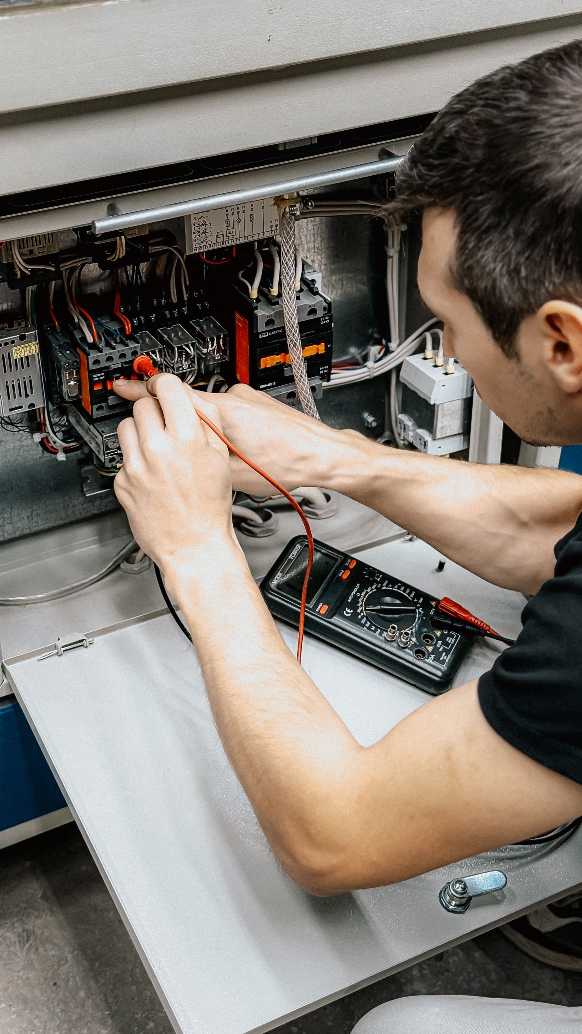 A tradesperson using a multimeter to test a control panel inside an electrical switchboard